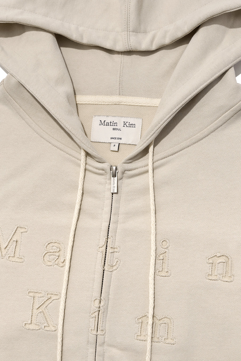 [matinkim] APPLIQUE CUTTED LOGO HOODY ZIP UP IN BEIGE