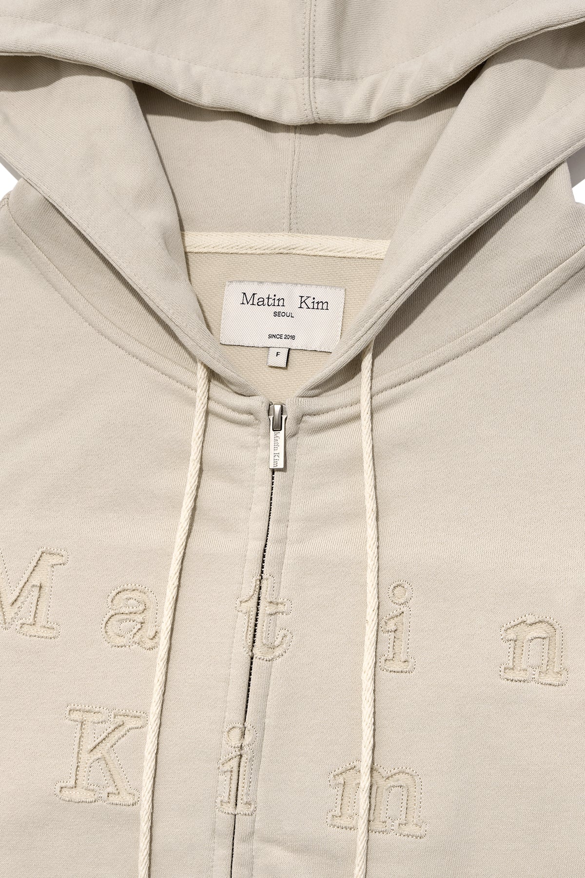 [matinkim] APPLIQUE CUTTED LOGO HOODY ZIP UP IN BEIGE